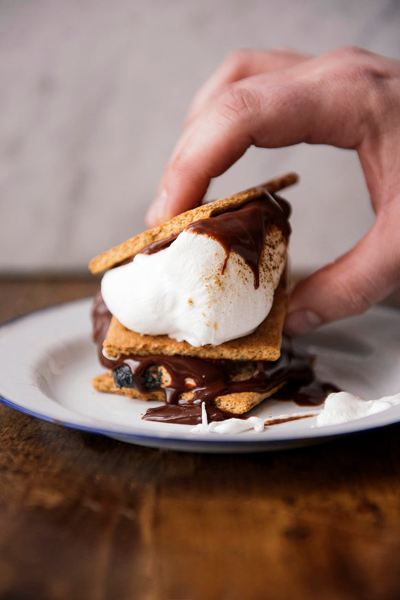 Hand holding a s'mores dessert on a white plate with a blurred background