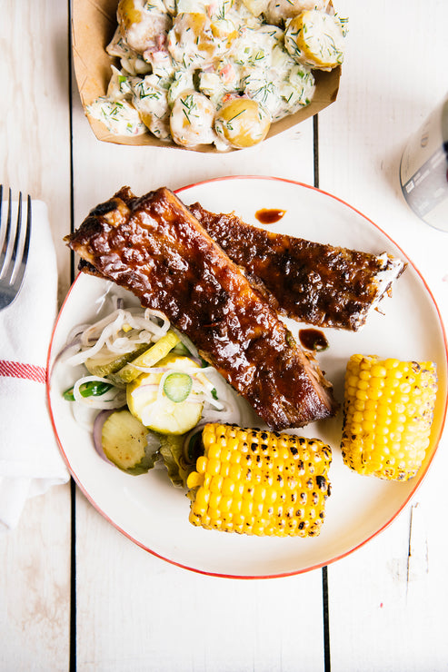 Load image into Gallery viewer, a plate of grilled pork ribs with bbq sauce and corn on the cob
