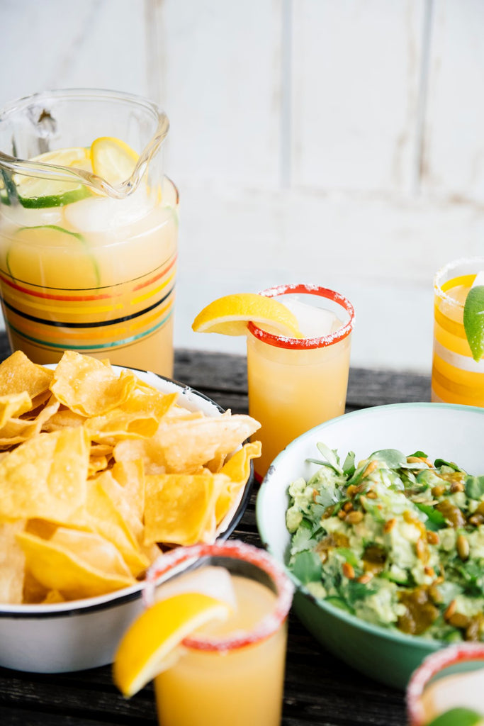 a bowl of homemade guacamole and chips next to a pitcher of margaritas