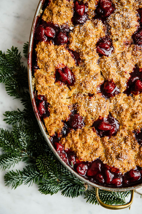 A Christmas Cherry cobbler in an oval baking pan with evergreen boughs surrounding it.