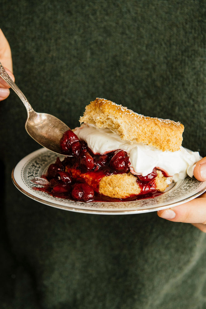 a person in a green sweater eating christmas cherries with biscuits and whipped cream