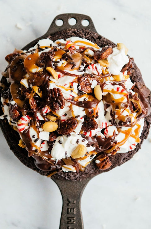 Load image into Gallery viewer, a skillet brownie with whipped cream, peppermint caramel, fudge sauce, candied pecans, and starlight candies
