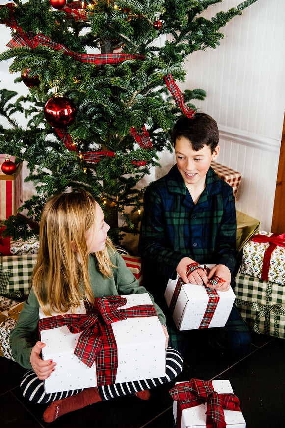 two children in front of a christmas tree opening gifts