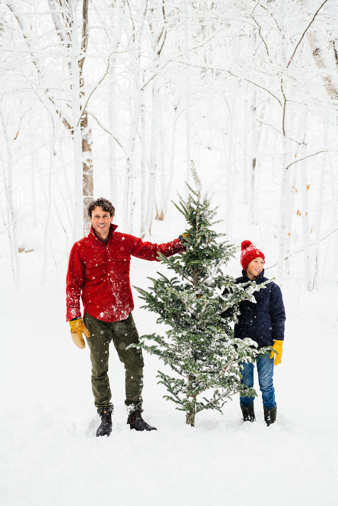 a dad and son with a christmas tree in a snowy forest