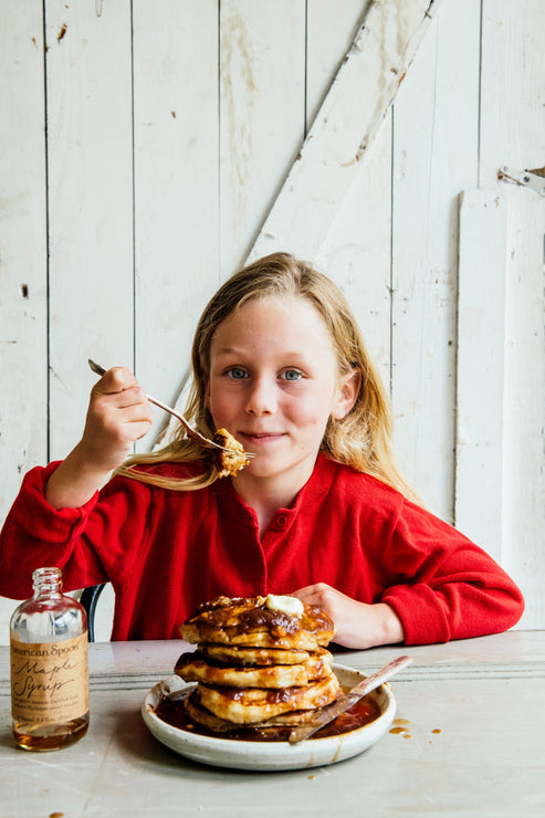 Load image into Gallery viewer, a young girl eating a stack of pancakes with maple syrup
