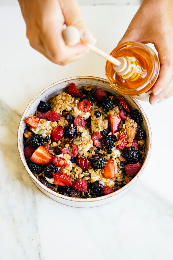 Bowl of granola and fruit with jar of honey and honey dipper