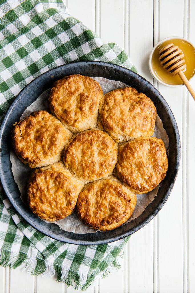 Skillet of homemade biscuits with honey dipper and honey set to the side.