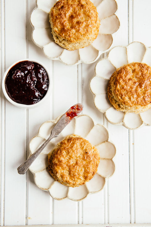 Three homemade biscuits on individual plates paired with a jar of preserves