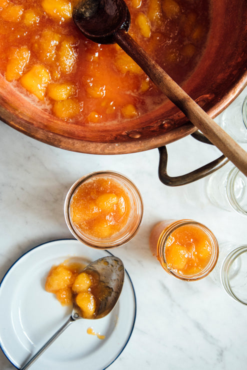 Load image into Gallery viewer, Copper kettle with peach preserves, two jars filled with peach preserves on a marble countertop.
