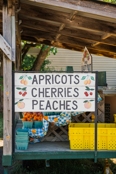 Load image into Gallery viewer, a sign at the farmers market reading &quot;apricots, cherries, peaches&quot; 
