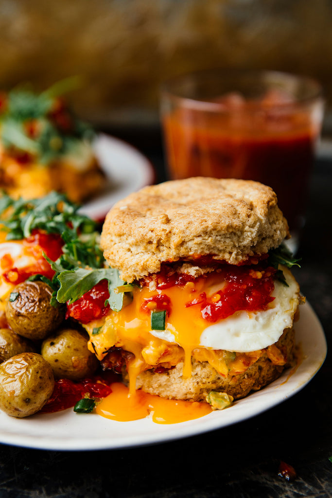 biscuit breakfast sandwich made with an egg, topped with chili jam alongside arugula and potatoes