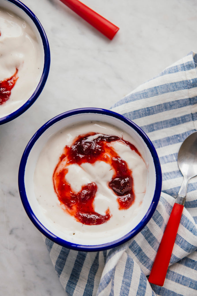 Two bowls of yogurt with strawberry preserves on a marble surface with a striped cloth and spoon.
