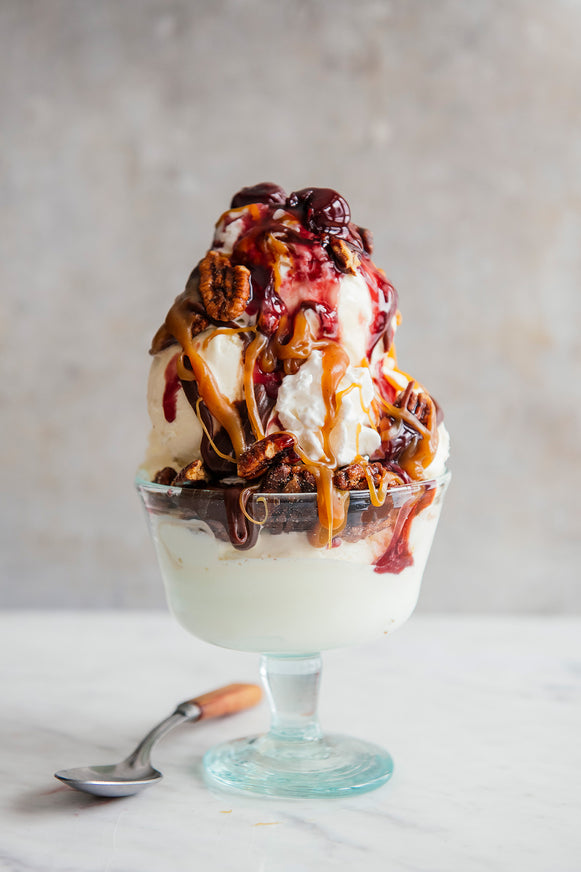 An ice cream sundae topped with cherries, pecans, caramel and fudge sauce