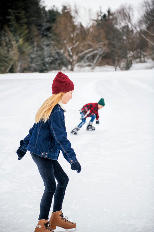 Load image into Gallery viewer, Girl in a ed beanie and blue jacket skating on a snowy ice rink.
