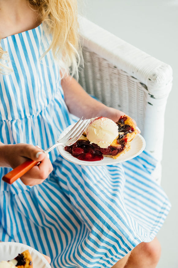 Girl in a blue and white striped dress holding a slice of pie with a fork.