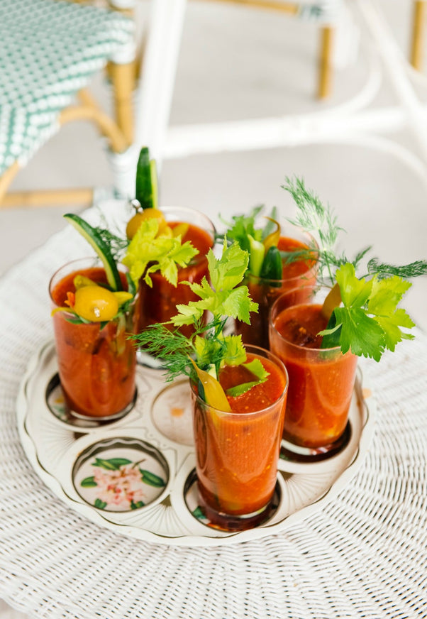 A vintage tray holding bloody marys, set on a wicker table.