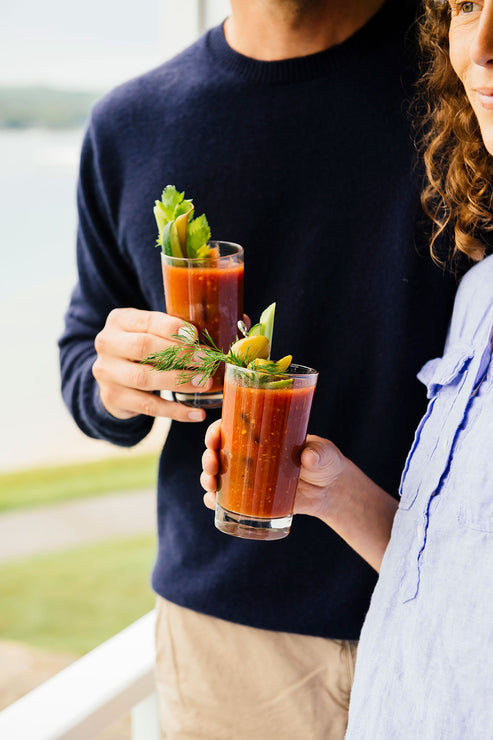 Load image into Gallery viewer, Two glasses of Bloody Mary cokctails topped with celery and herbs in a cheers
