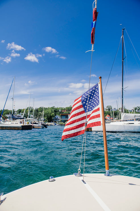 Load image into Gallery viewer, American flag on a boat with a marina and blue sky in the background
