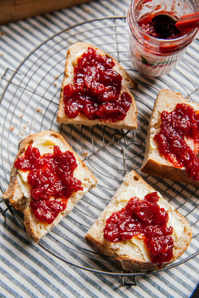 Three slices of bread with butter and sour chery preserves on a cooling rack, with a jar of preserves in the background.