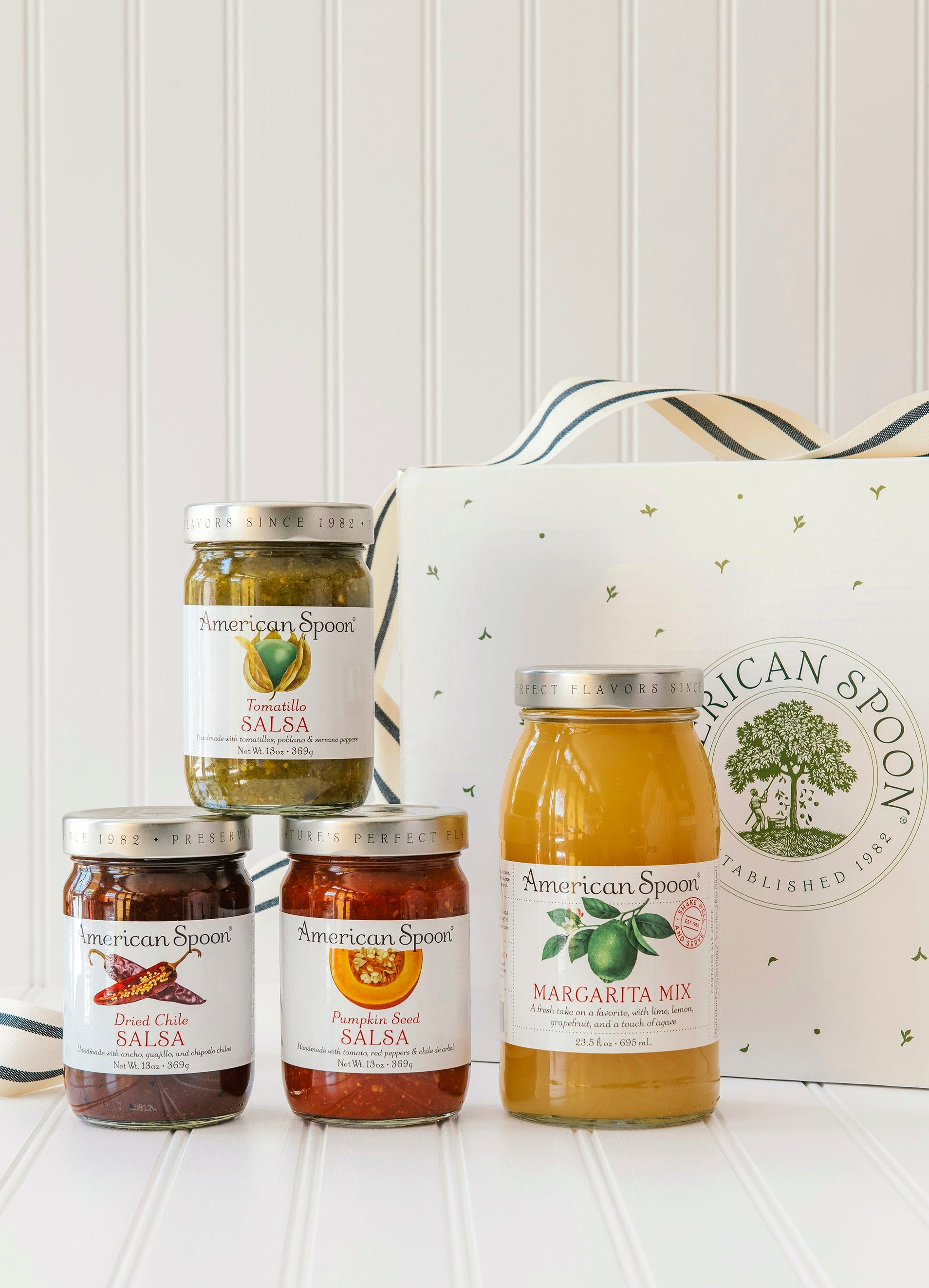 American Spoon Tomatillo, Dried Chili & Pumpkin Seed salsa and Margarita mix bottles with a branded box on a white surface.