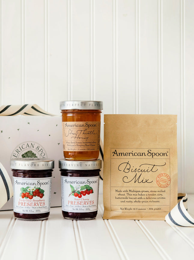 American Spoon Sour Cherry Preserves, Early Glow Strawberry Preserves, Star Thistle Honey and Biscuit Mix bottles with a branded box on a white surface.