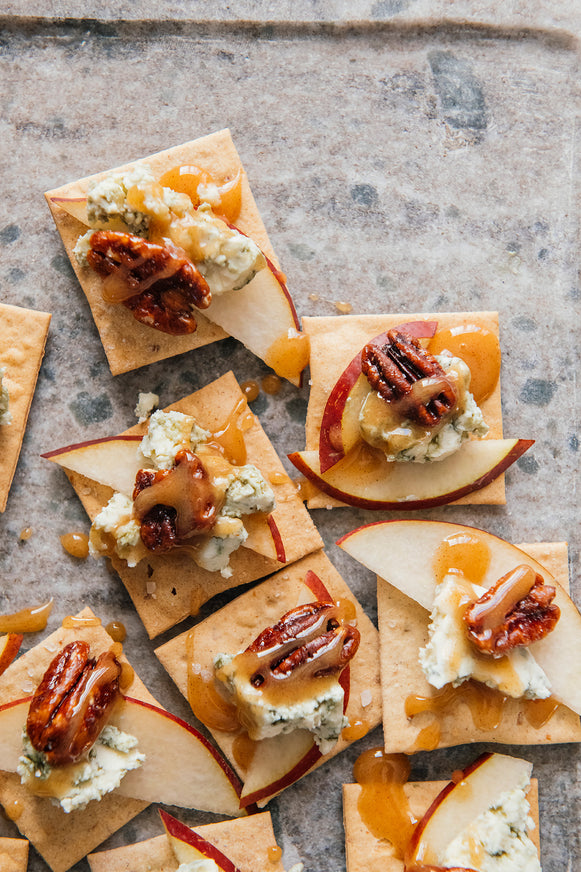 Crackers topped with cheese, apples, and Candied Pecans on a rustic surface
