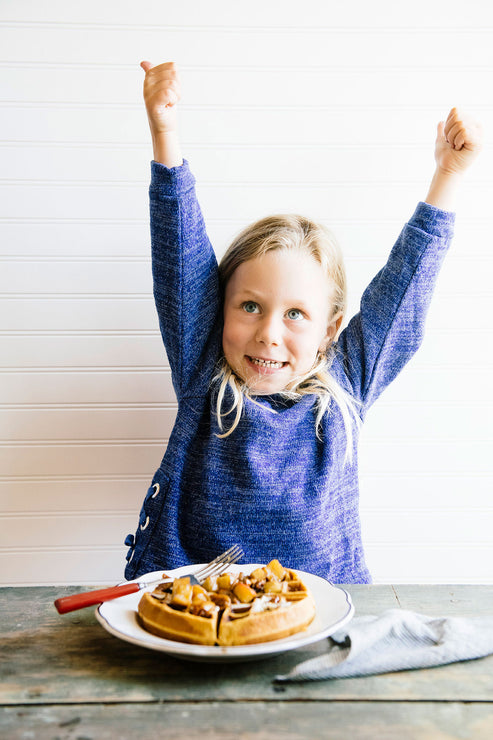 Load image into Gallery viewer, A young girl with her arms raised with thumbs up and a plate of waffles
