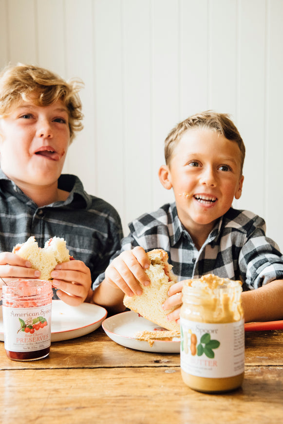 Two young boys eating Peanut Butter and preserve sandwiches 