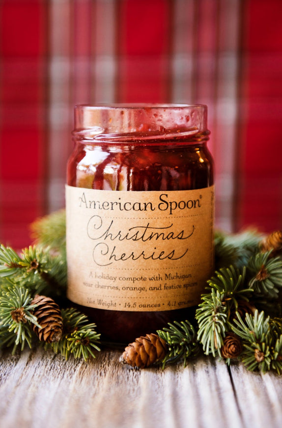 Open jar of Christmas Cherries surrounded by greenery and pinecones 