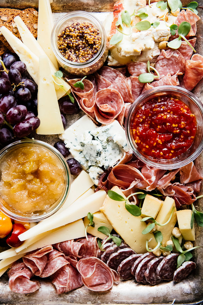 A charcuterie board of salamis and cheese with Bartlett Pear Preserves, Whole Seed Mustard and Chili Jam