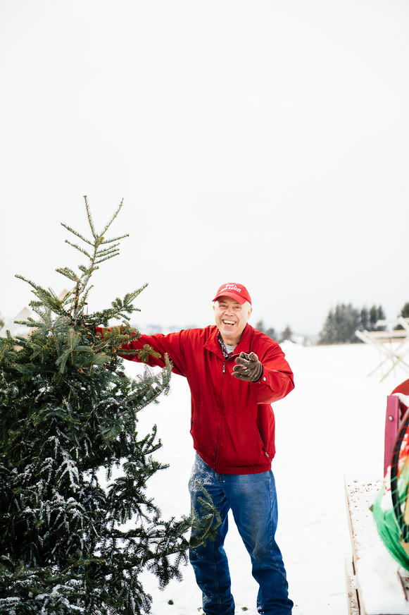 Bill McMaster of Bill's Farm Market shaking snow off of a Christmas Tree