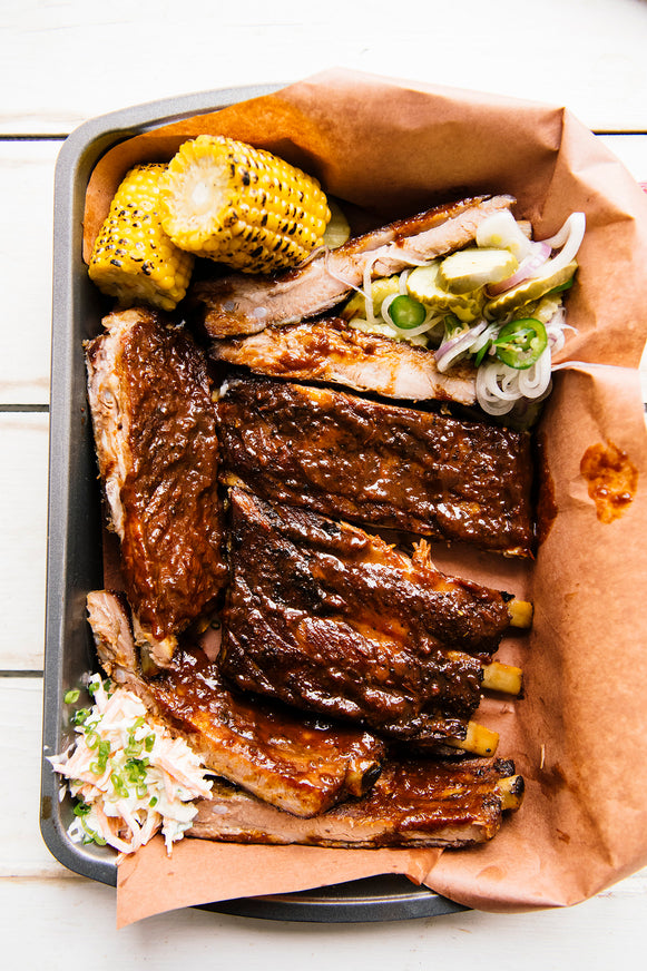 A rack of ribs with homemade pickles and corn on the cob