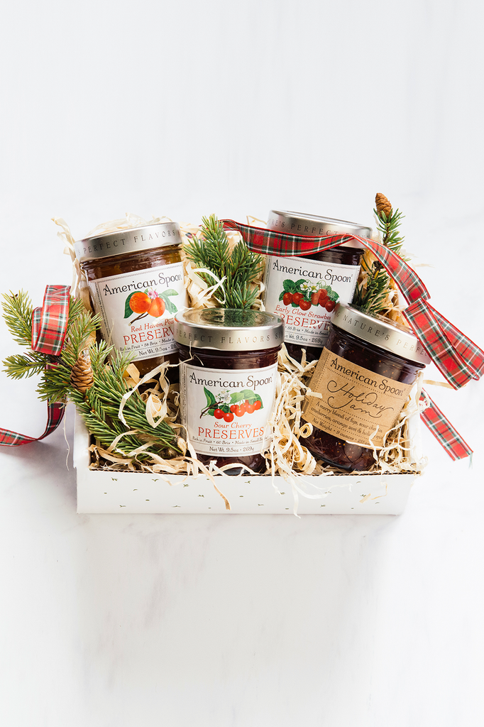A Holiday Jam gift box containing Sour Cherry Preserves, Early Glow Strawberry Preserves, Red Haven Peach Preserves and Holiday Jam with holiday ribbon and greenery