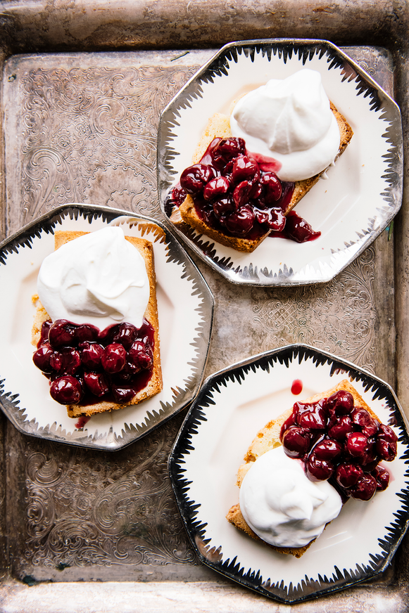 Three plates with individual slices of pound cake topped with Christmas Cherries and fresh whipped cream