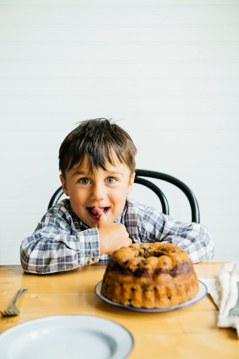 Load image into Gallery viewer, A young boy sitting at a table with a small Blueberry Coffee Cake plated in front of him
