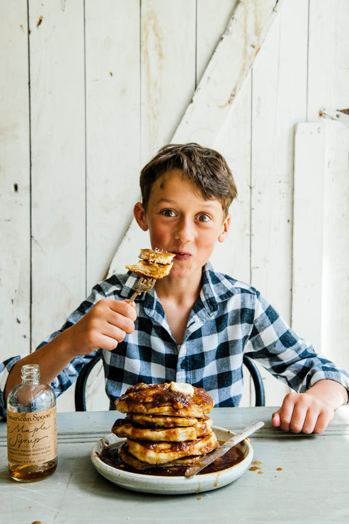 Load image into Gallery viewer, A young boy with a fork full of pancakes and a stack of pancakes covered in Maple Syrup
