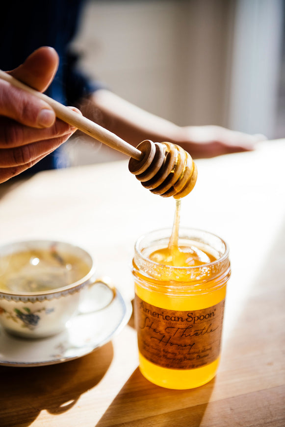 A jar of Star Thistle Honey with a honey dipper and cup of tea