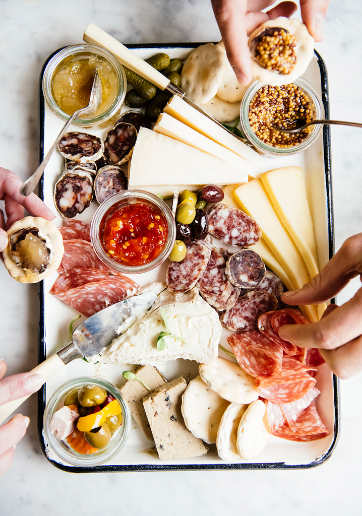 A charcuterie board of sliced salamis, cheese, Wholeseed Mustard, Chili Jam and Bartlett Pear Preserves