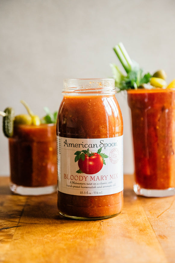 A jar of Bloody Mary Mix with two glasses of homemade bloody mary's in the background