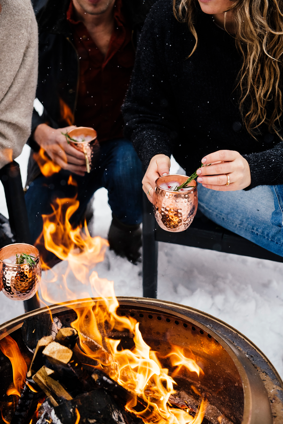 Friends holding copper cups with hot toddy's around a fire outside in the snow